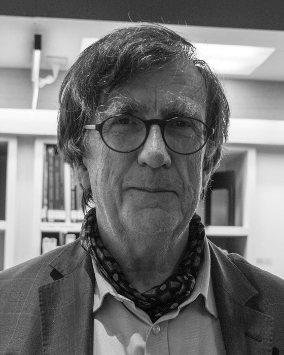 Bruno Latour in glasses and a patterned scarf, in front of bookshelves
